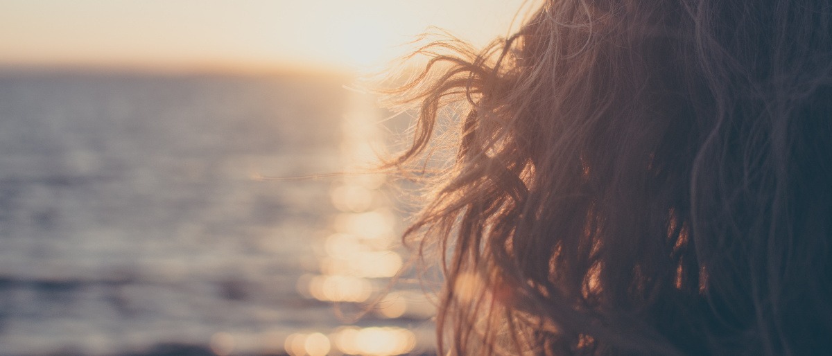 Eine Frau mit langen Haaren sitzt am Meer