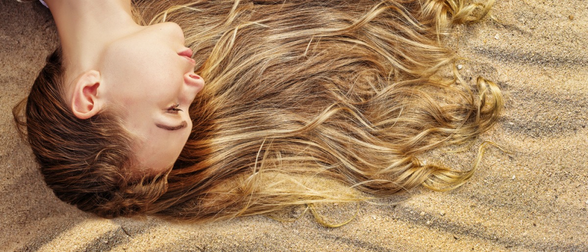 Eine Frau liegt mit ihrer Frisur am Sandstrand im Sommer