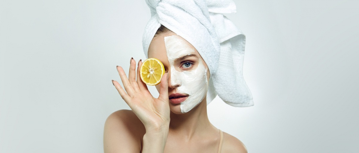 Frau mit Creme im Gesicht und Zitrone in der Hand