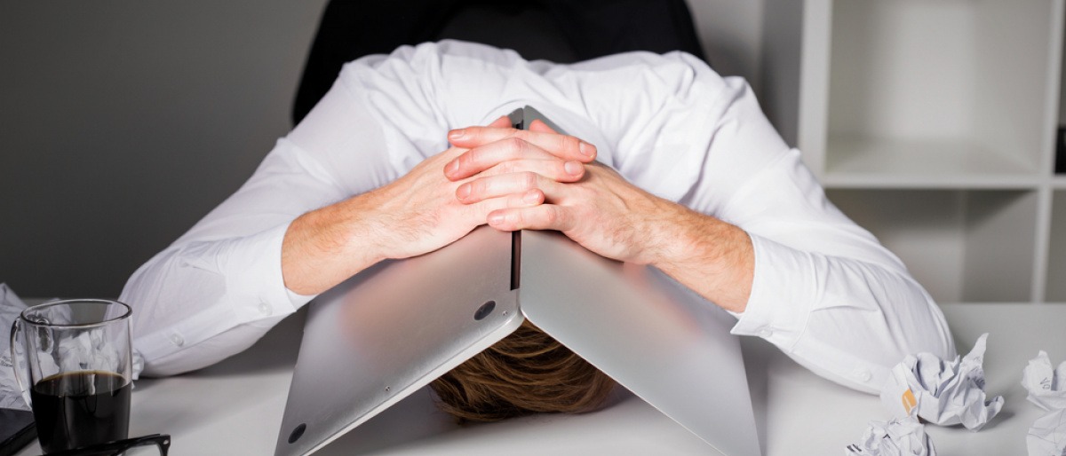 Ein frustrierter Mann versteckt sein Gesicht unter einem Laptop