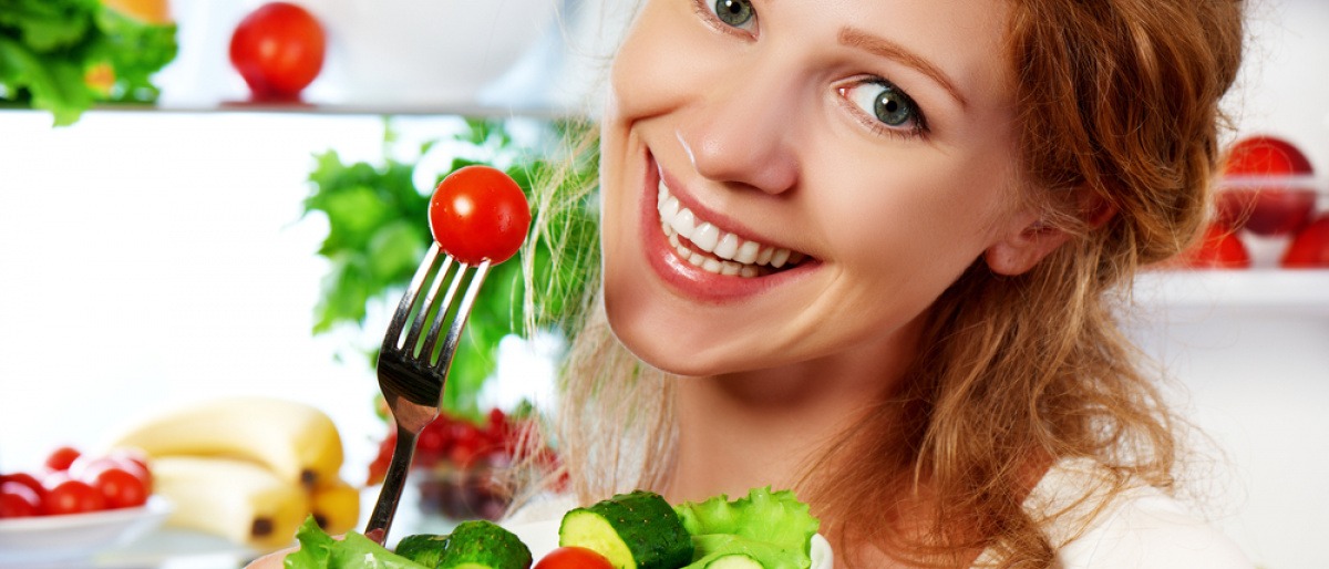 Frau ist Salat und Tomaten als gesunde Ernährung vor einem Kühlschrank