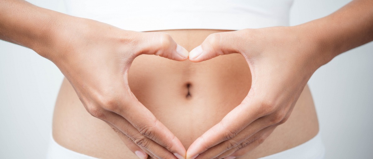 Frau formt Herz über dem Bauch.