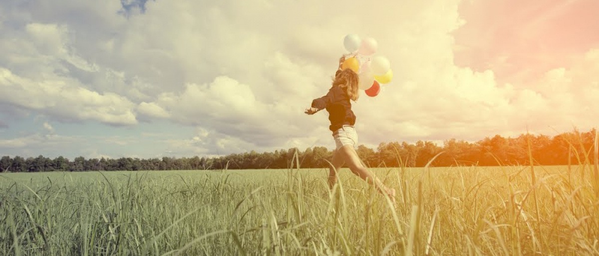 Eine Frau läuft mit Ballons durchs Feld und will glücklich sein