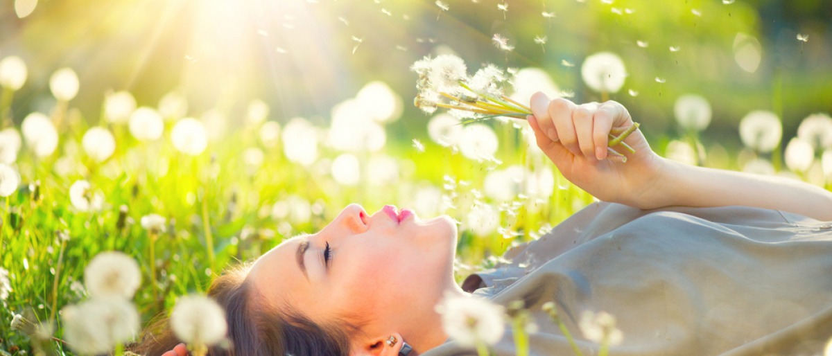 Eine Frau pustet glücklich auf eine Pusteblume