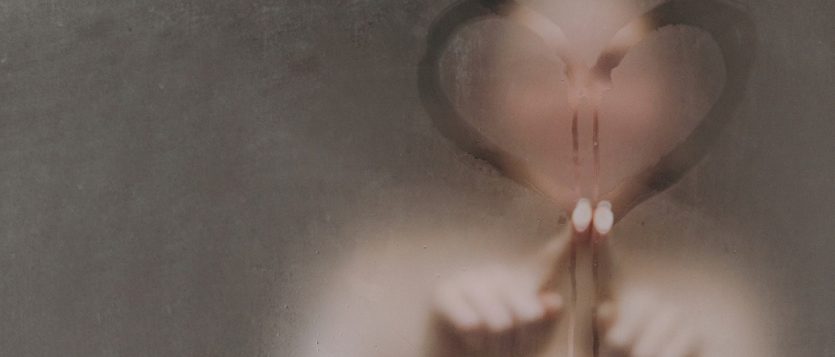 Frau in der Dusche malt Herz an beschlagene Duschwand aus Glas.