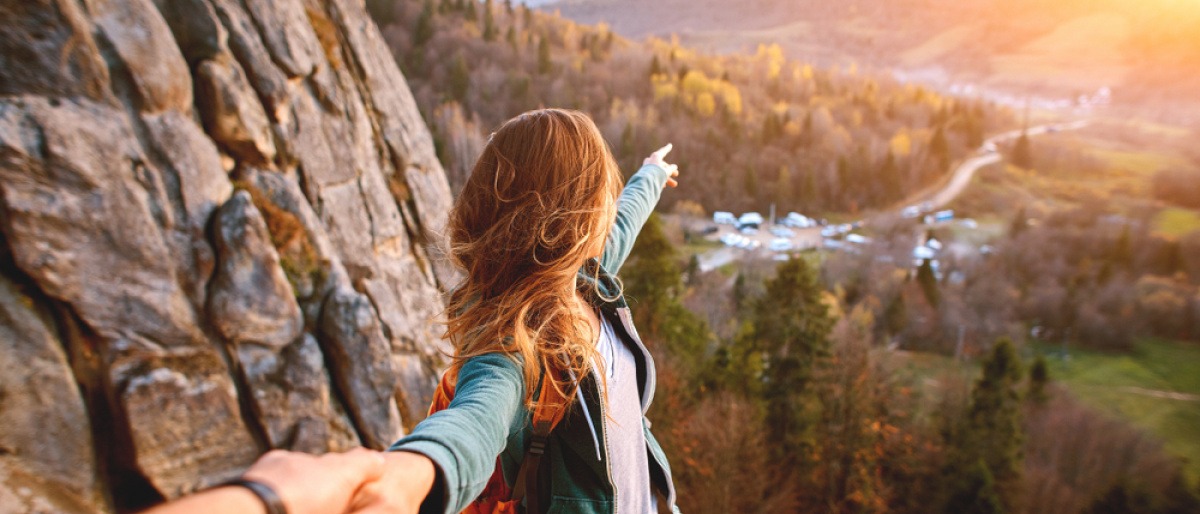 Horizont erweitern - junges Paar beim Wandern auf einem Berg, die Frau zeigt in Richtung Horizont.