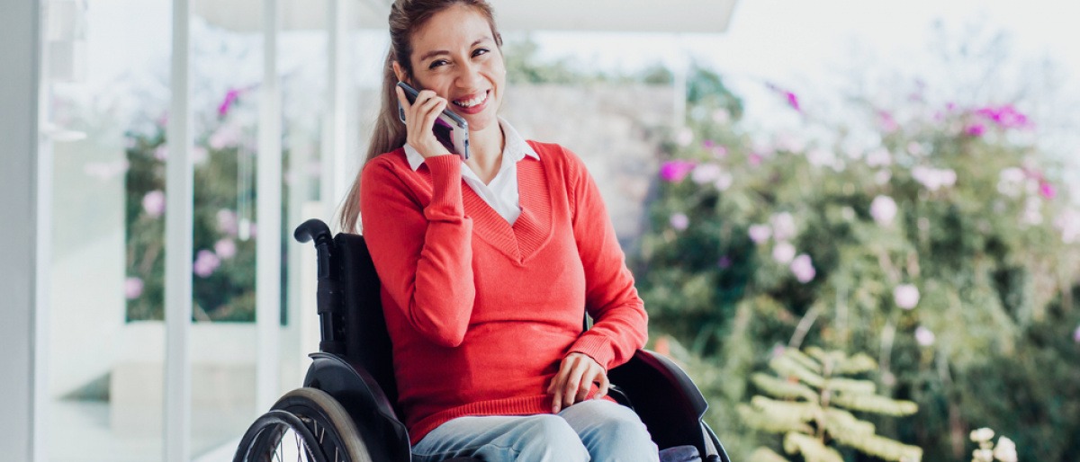 Eine Frau sitzt im Rollstuhl und telefoniert glücklich