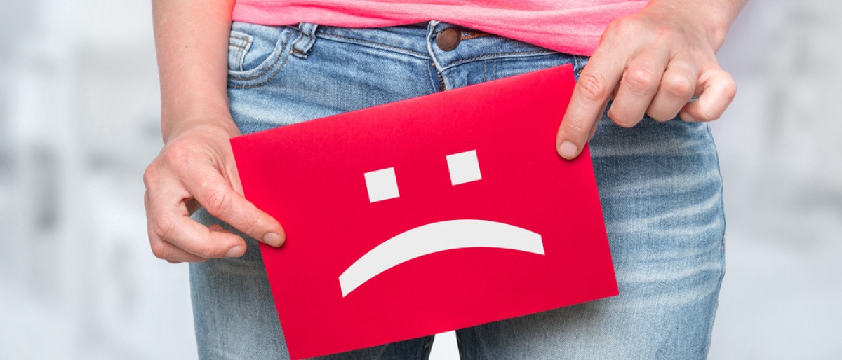 Frau hält Schild mit traurigem Smiley als Zeichen für Inkontinenz