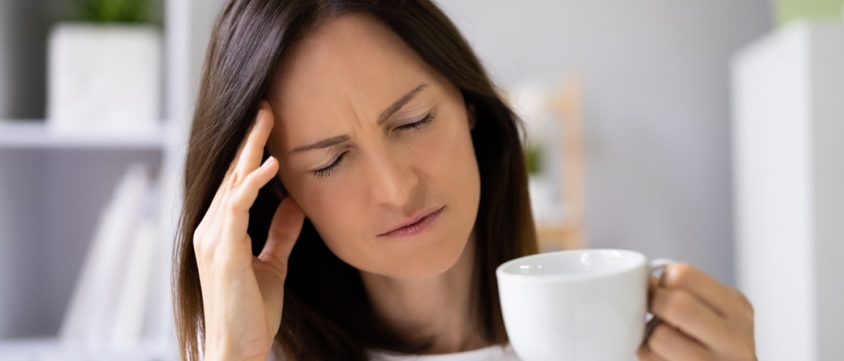 Frau mit Kopfschmerzen hält Tasse mit Kaffee