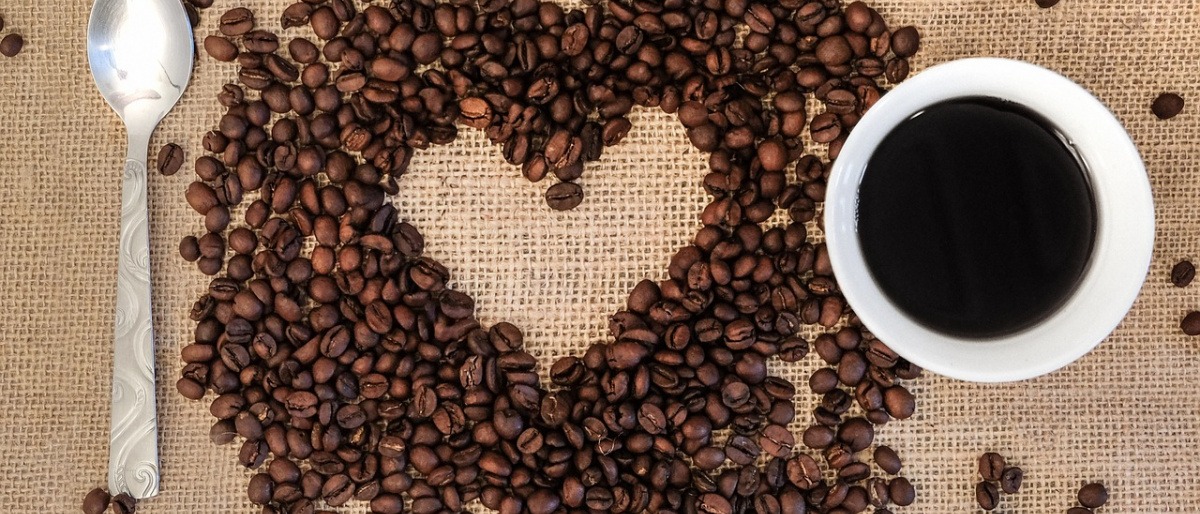 Neben einer Kaffeetasse liegen Kaffeebohnen und ein Löffel