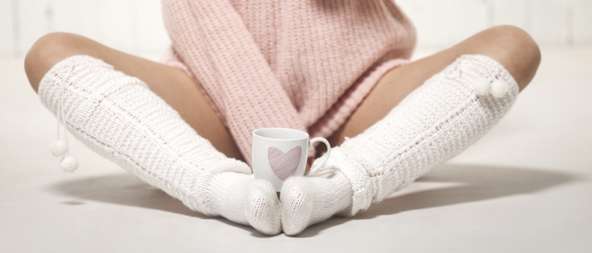 Eine Frau wärmt ihre kalten Hände und kalten Füße an einer Tasse Tee