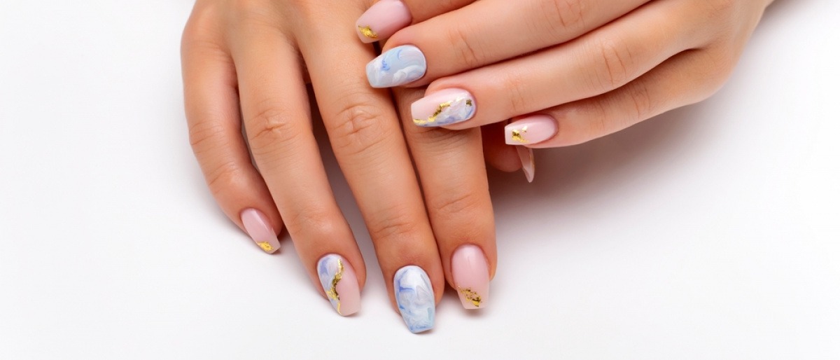 Kintsugi Nails - Nahaufnahme einer Frau, die sich ihre goldbemalten Finger vor das ebenfalls mit Goldfarbe dekorierte Gesicht hält.