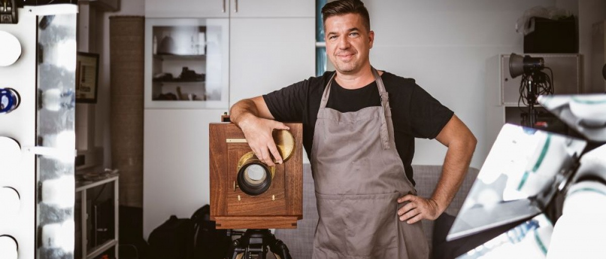 Der Fotograf Erik Diewald steht neben einer Großformatkamera aus Holz