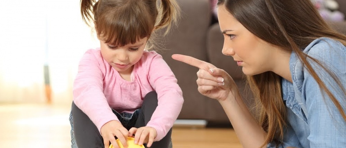 Eine Mutter ermahnt ihr spielendes Kleinkind mit erhobenem Zeigefinger. 