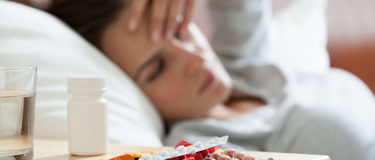 Eine Frau mit Krankheit liegt im Bett mit Tabletten daneben