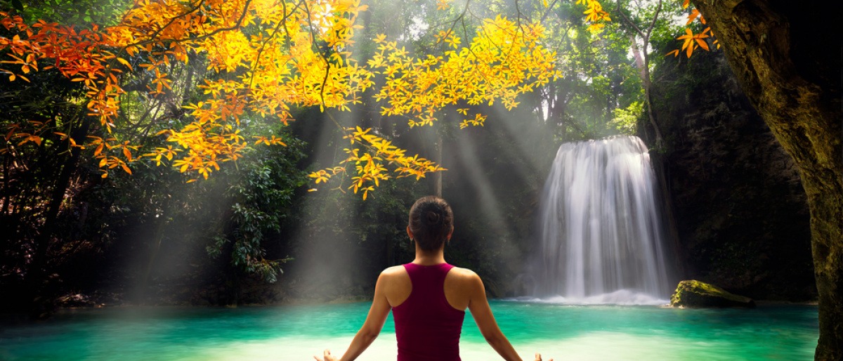 Eine Frau sitzt in einer herbstlichen Landschaft und macht Yoga