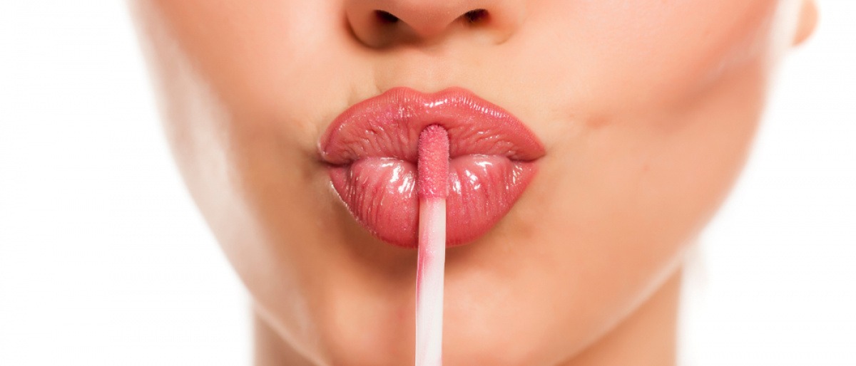Frau macht einen Kussmund und hält einen Lipgloss an die Lippen
