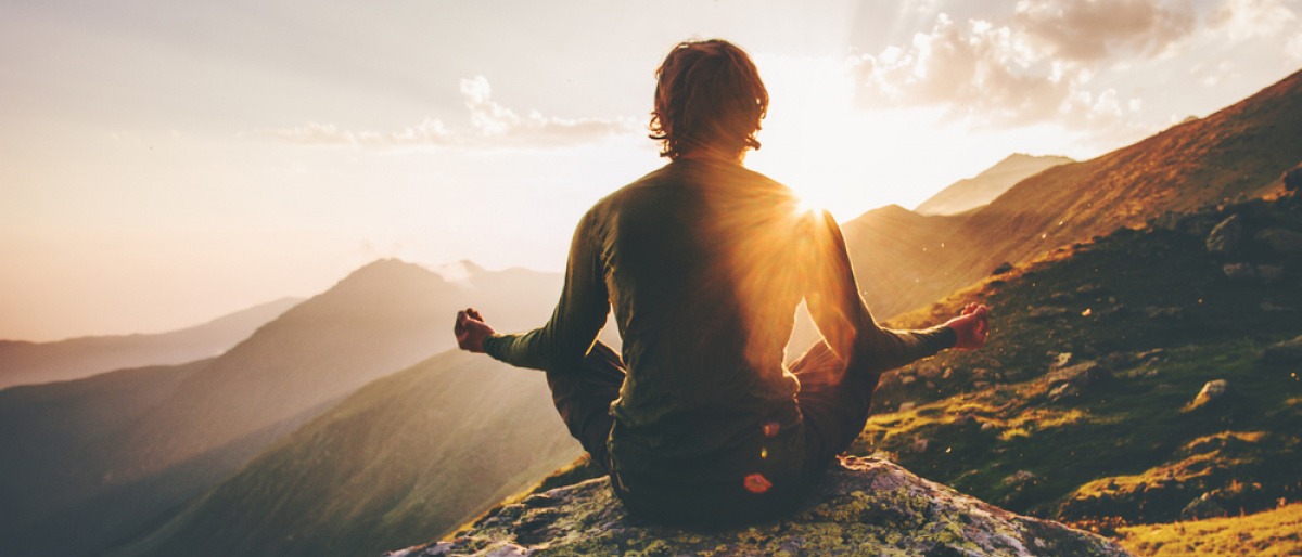 Ein Mann sitzt im Schneidersitz auf einem Berg und meditiert