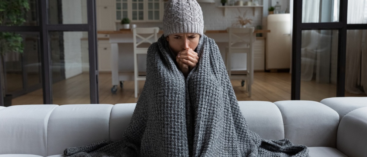 Frau sitzt mit Decke und Mütze auf dem Sofa