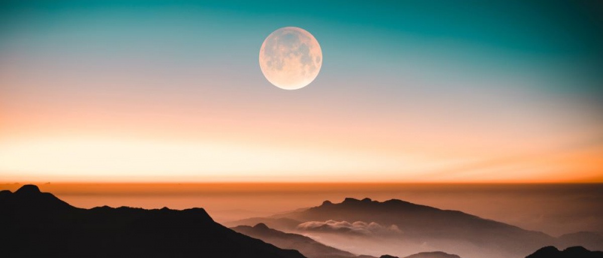 Im Hintergrund einer Berglandschaft befindet sich der Mond