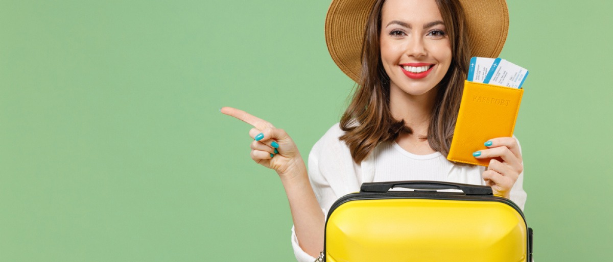 Nachhaltig reisen - junge lächelnde Frau mit gepacktem Koffer und zwei Flugtickets in der Hand. 