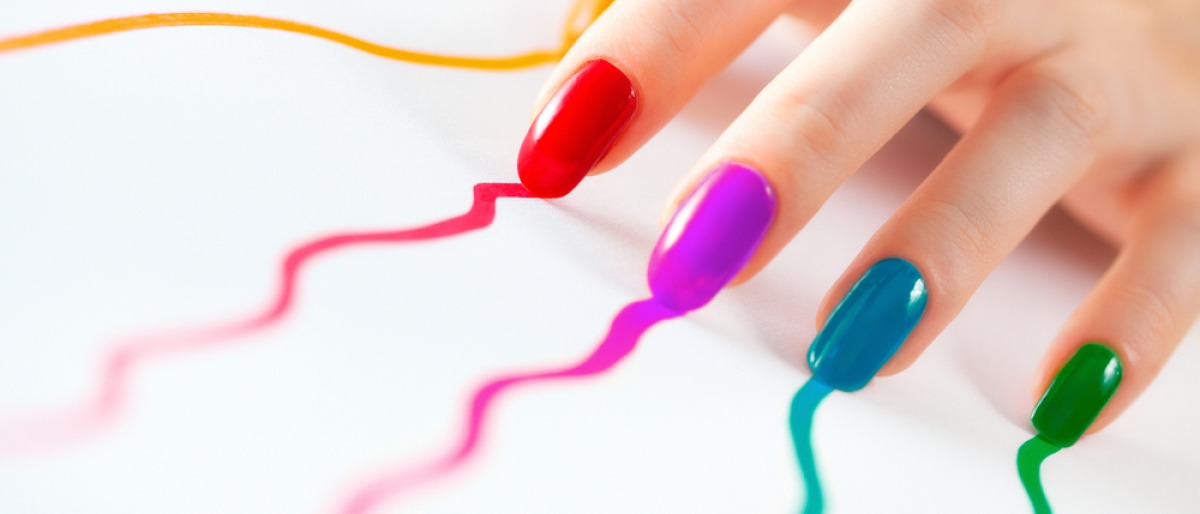 Finger mit Nagellack in Regenbogenfarben hinterlassen auf einem Blatt Papier die Farbe