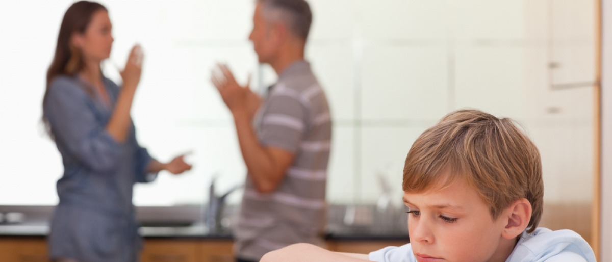 Eltern verbreiten in einer Küche negative Emotionen durch einen Streit, ein Junge sitzt im Vordergrund