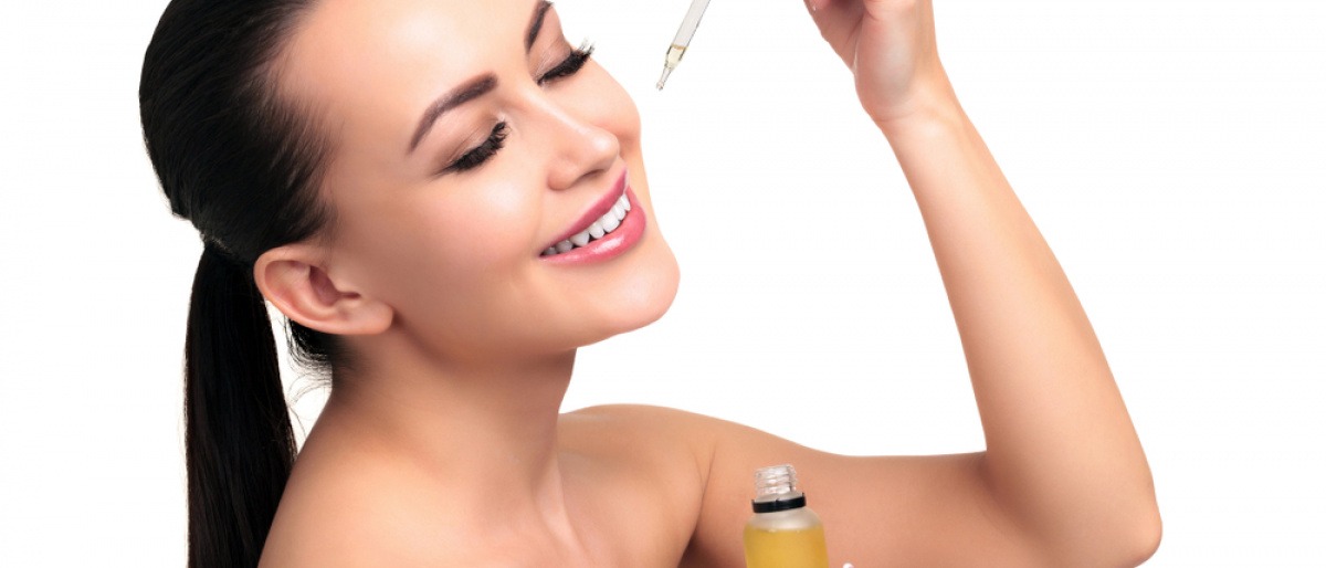 Frau gibt mit einer Pipette Olivenöl ins Gesicht