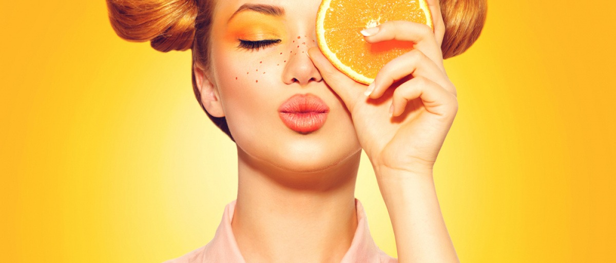 Eine Frau hält sich eine Orangenhälfte vor das Gesicht
