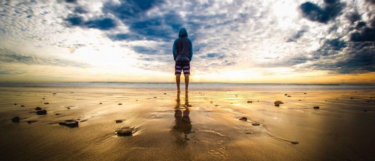 Eine Person steht am Strand unter einem dunklen Wolkenhimmel in einer besonderen Atmosphäre