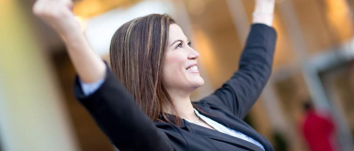 Eine Frau in einem Businessoutfit reckt triumphierend die Arme in die Luft und wirkt glücklich. Es scheint, als wüsste sie genau, wie sie ihr Potential entwickeln und nutzen kann.