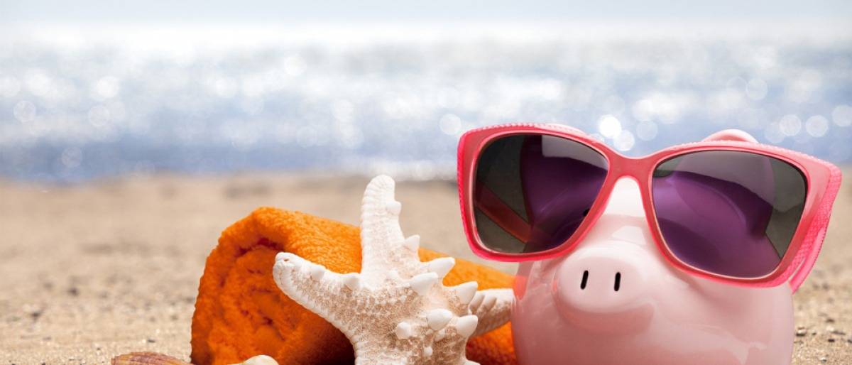 Ein Sparschwein ist auf einem Strand und Utensilien zum Reisen