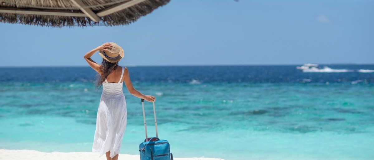 Frau mit Reisekoffer am Strand als Reiseziel im Juli