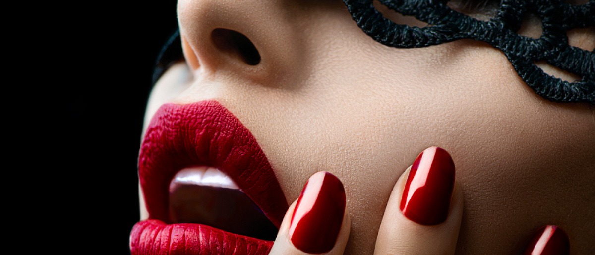 Eine Frau mit dunklem Haar trägt einen roten Lippenstift und klassische rot lackierte Fingernägel