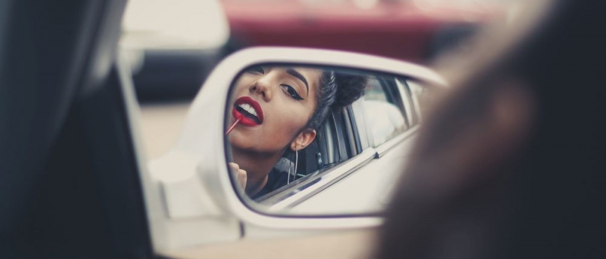 Eine Frau trägt sich im Auto roten Lippenstift auf