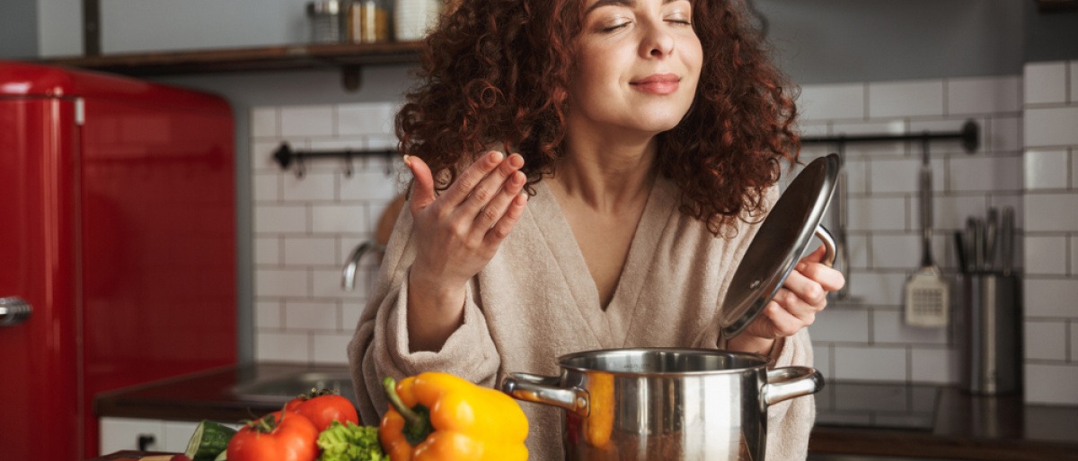 Frau genießt Duft aus Kochtop, daneben liegt Gemüse