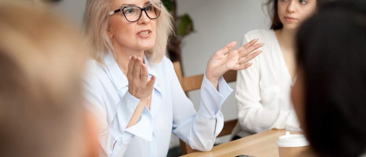 Eine ältere Frau diskutiert mit anderen Menschen an einem großen Tisch.