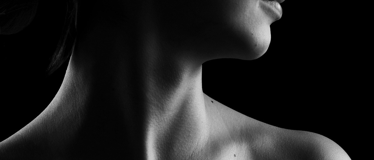 Eine Frau zeigt ihren Hals, wo die Schilddrüse sitzt