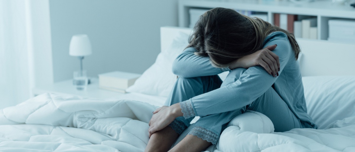 Frau im Schlafanzug sitzt mit Schlafproblemen wegen Störfeldern im Bett
