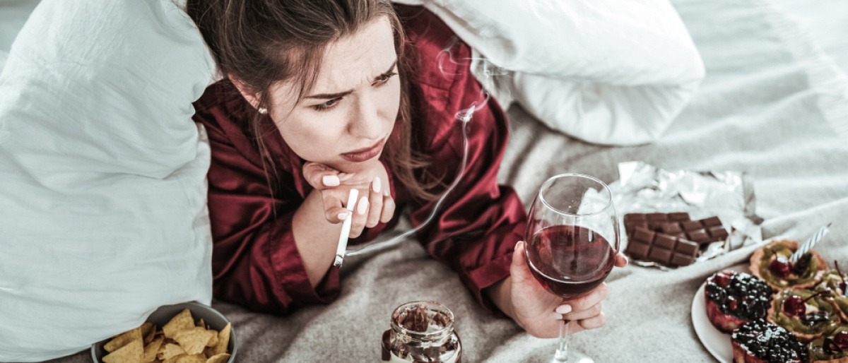 Eine Frau liegt im Bett, trinkt Wein, raucht und will schlechte Gewohnheiten loswerden.