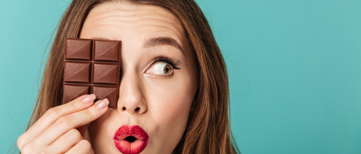 Frau hält sich eine Tafel Schokolade vor das Gesicht. 