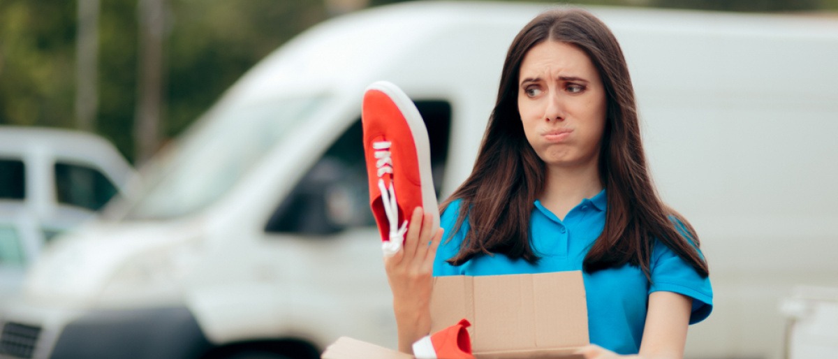 Frau mit enttäuschtem Gesichtsausdruck läuft mit einem Karton mit Schuhen, die quietschende Sohlen haben, durch die Gegend. 