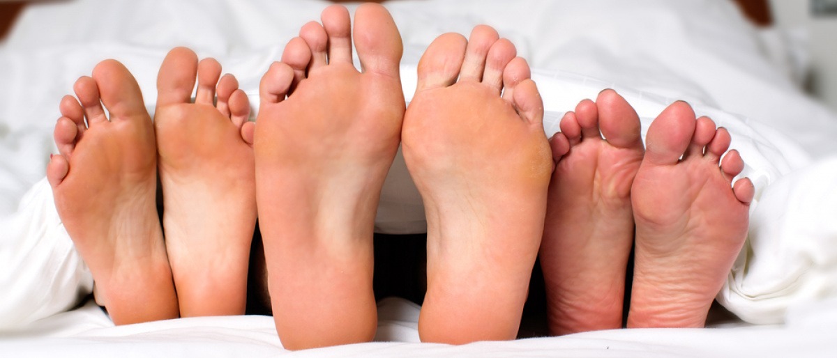 Drei Paare von Füßen unter einer Bettdecke.