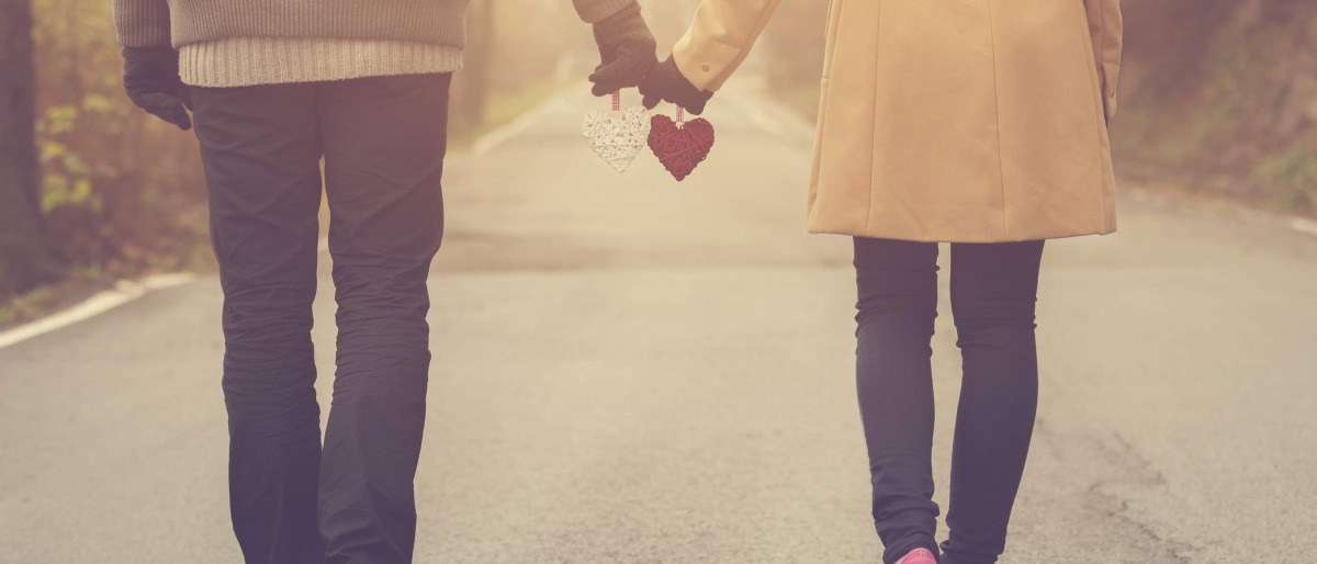 Ein Paar, das Hand in Hand mit jeweils einem Herz in der Hand einen Spaziergang macht
