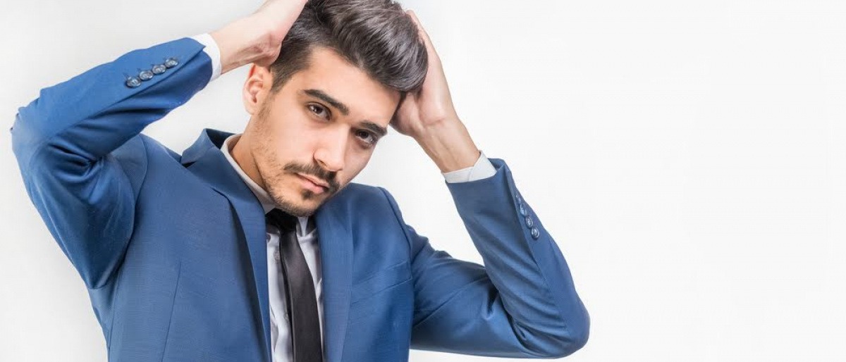 Ein Mann mit hoch gestyltem dunklem Haar hebt sich beide Hände ins Haar