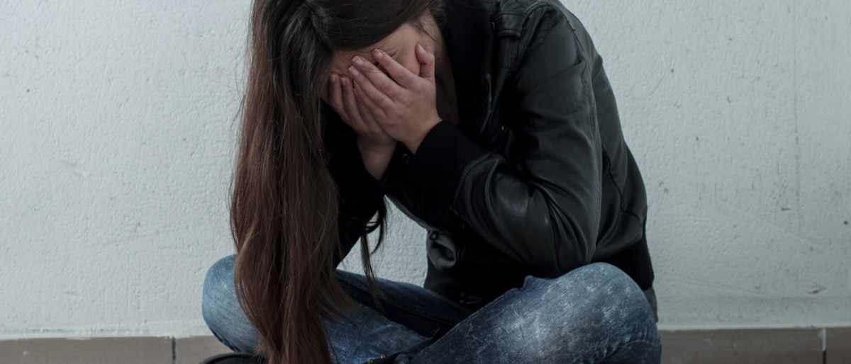 Sich selbst im Weg stehen - junge Frau im Schneidersitz auf Boden, gesenkter Kopf, Gesicht in den Händen vergraben.