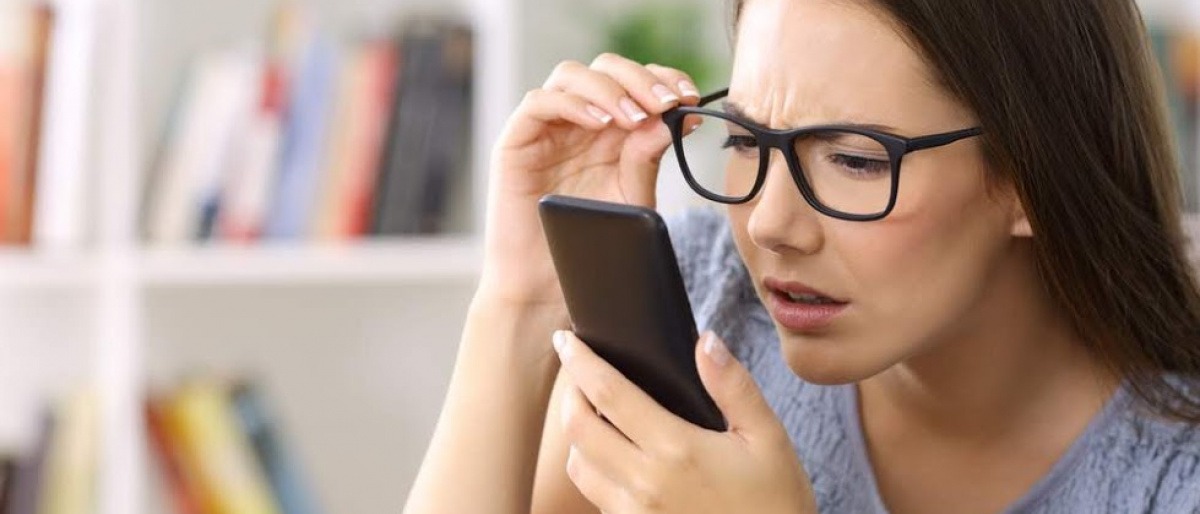 Eine Frau hält die Brille hoch, während sie auf ihr Smartphone sieht