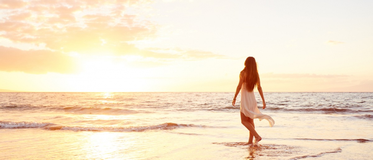 Eine Frau geht im Sonnenuntergang am Strand spazieren