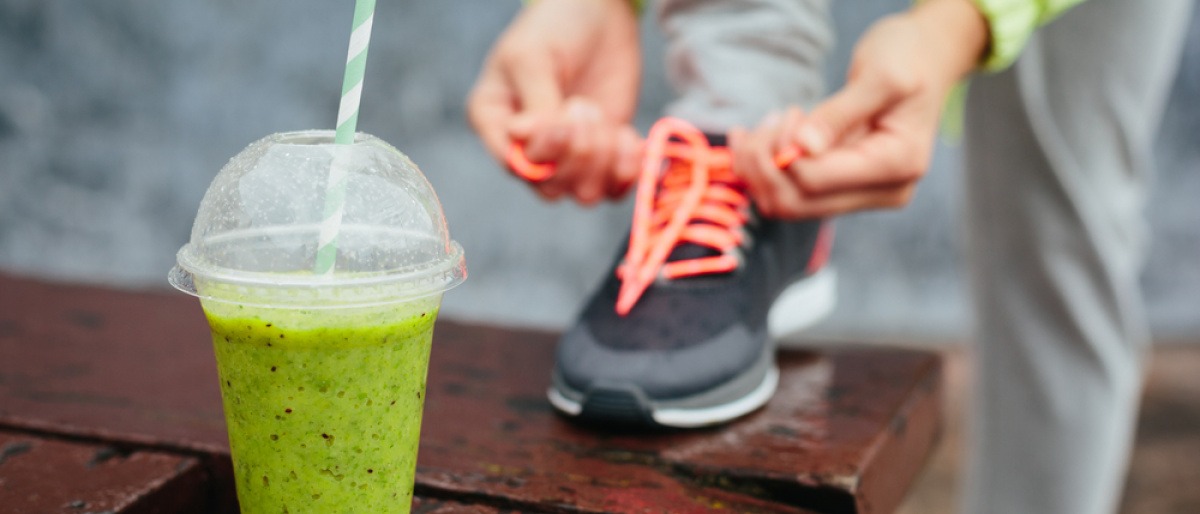 Jemand bindet ein Schuhband eines Sportschuhs, ein Smoothie ist im Vordergrund