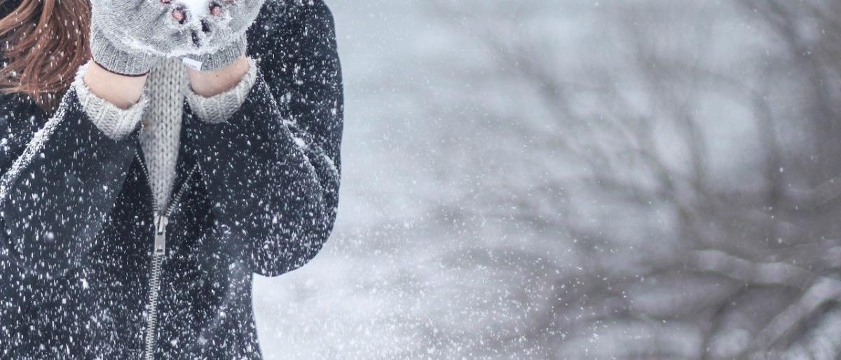 Eine Frau mit starkem Immunsystem bläst im Winter Schnee von den Händen